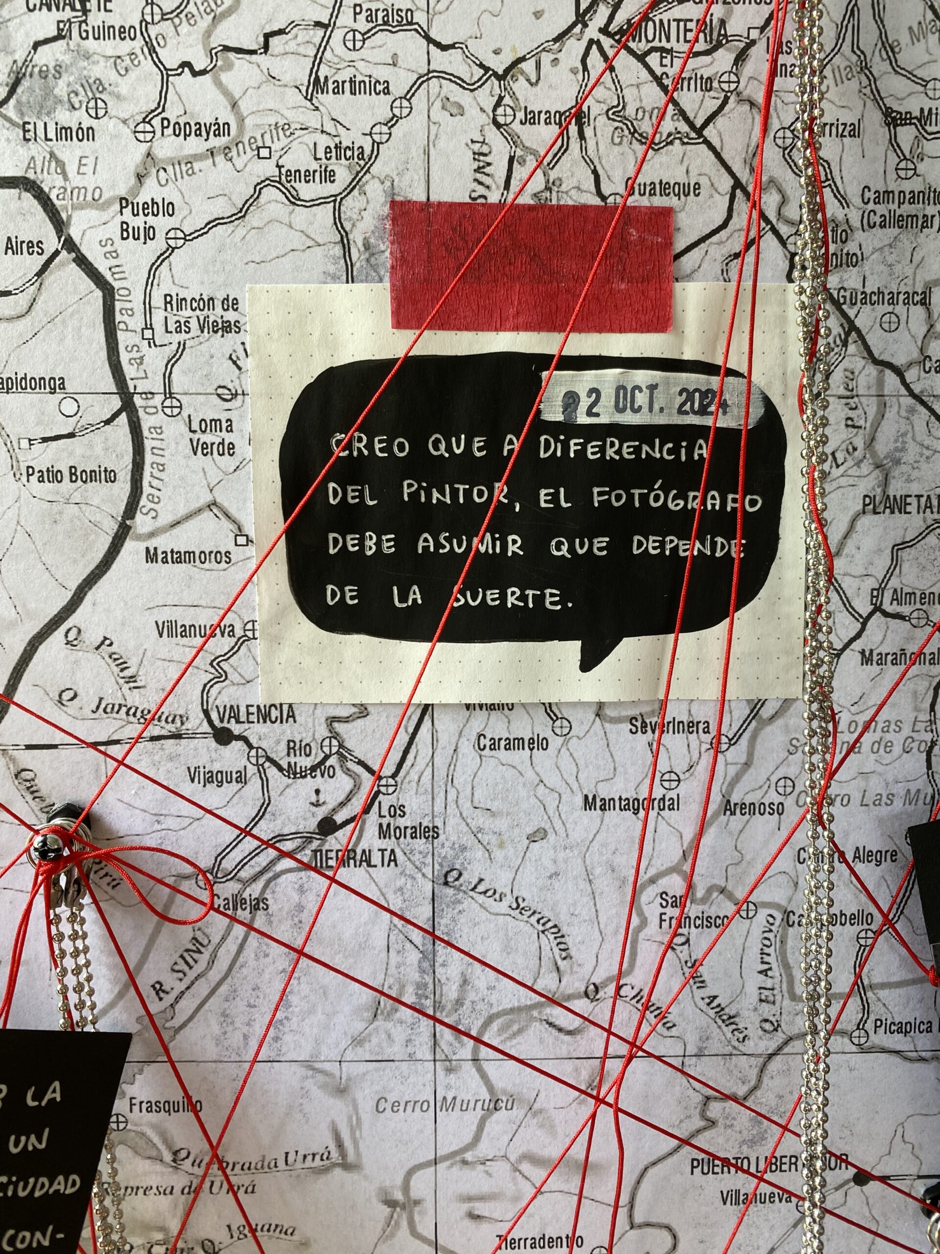 Detalle de la instalación Días de la cosecha de Delio Aparicio: mapa de Antioquia intervenido con hilos rojos y una cita manuscrita sobre fotografía y suerte.